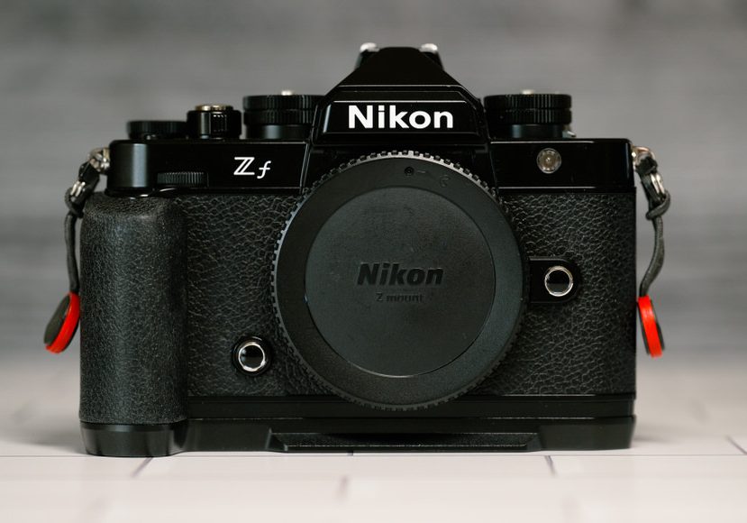 A Nikon Zf camera without a lens, displayed on a table, showcasing its front view with a black body and grip. A Nikon Zf camera without a lens, displayed on a table, showcasing its front view with a black body and grip.