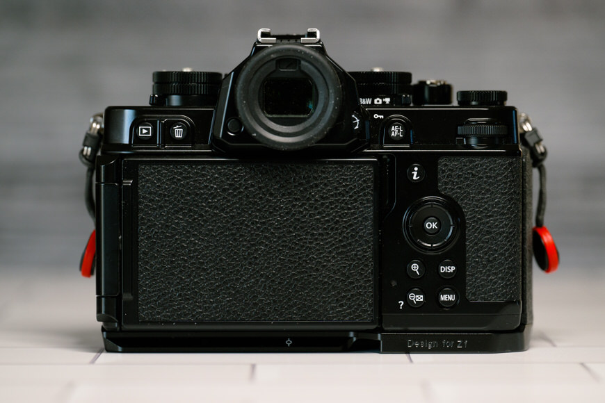 Back view of a black digital camera with a textured grip and various control buttons, placed on a light surface.