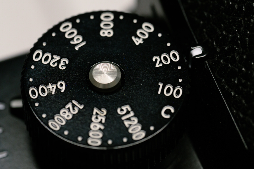 Close-up of a black camera ISO dial, displaying settings from 100 to 51200 in white text.