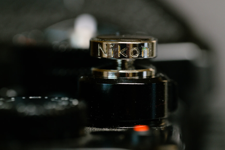 Close-up of a Nikon camera shutter button, showing metallic texture and engraved brand name.