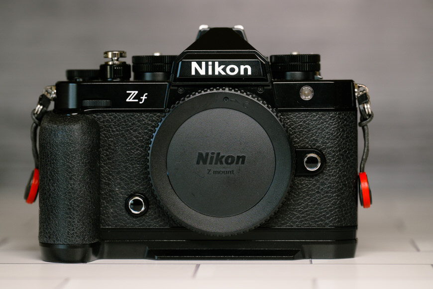 Front view of a Nikon Zf camera with a textured grip and lens cap on a tiled surface.