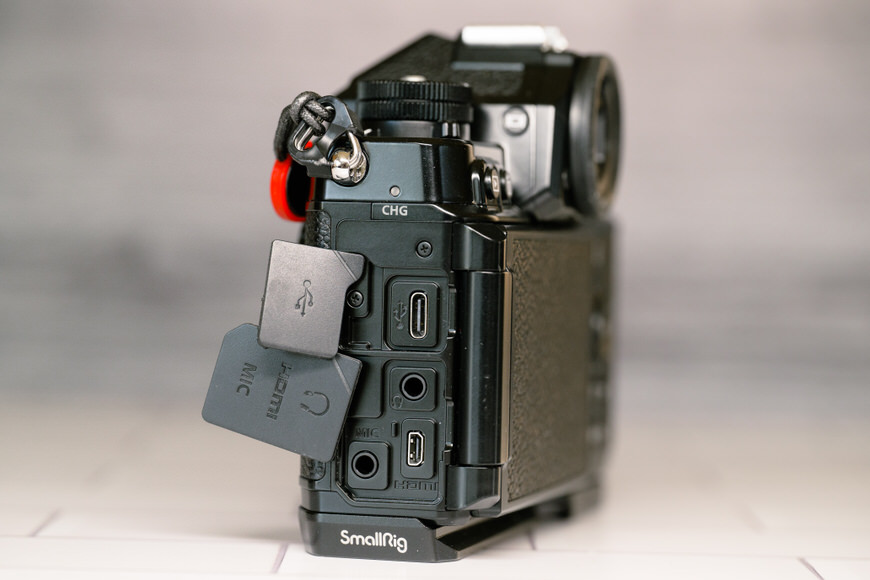 Camera with open side panels showing USB, HDMI, mic, and headphone ports. Two SD cards are partially inserted. The camera is mounted on a SmallRig bracket.