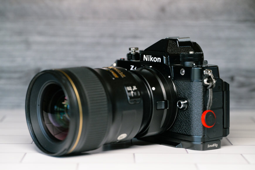 A Nikon Z camera with a large lens attached rests on a tiled surface against a gray background.