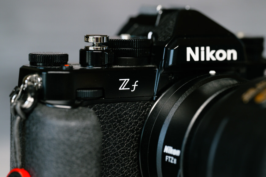 Close-up of a Nikon Z f camera, showing the Z f logo and part of the lens with a blurred background.