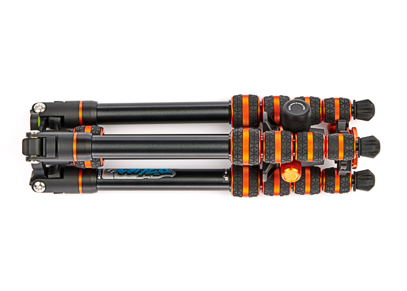 A compact black and orange tripod with folded legs and adjustable knobs, featuring rubber grips and metal components.