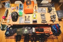 A table displays organized hiking and photography gear, including backpacks, clothing, camera equipment, hydration packs, and a helmet.