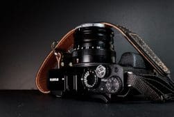A Fujifilm camera with a leather strap attached, placed on a black surface.