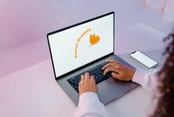 Person typing on a laptop with "Sweet Dreams" and a cartoon fox on the screen. A smartphone is placed to the right of the laptop on the desk.