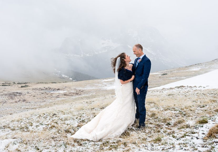 A couple in wedding attire stand on a snowy mountain landscape, smiling at each other with mist-covered peaks in the background. A couple in wedding attire stand on a snowy mountain landscape, smiling at each other with mist-covered peaks in the background.