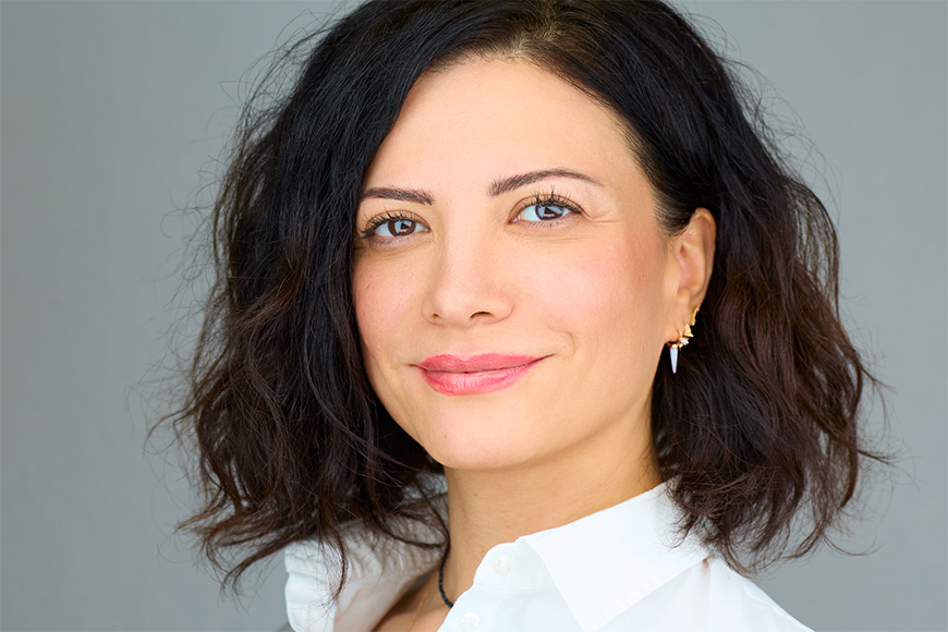 Woman with shoulder-length dark hair wearing a white shirt, smiling slightly against a plain background.