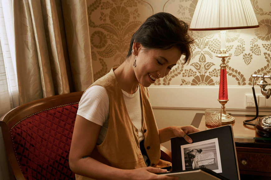 A person sitting in a chair, looking at a photo album with a glass of water and a lamp on a table beside them.