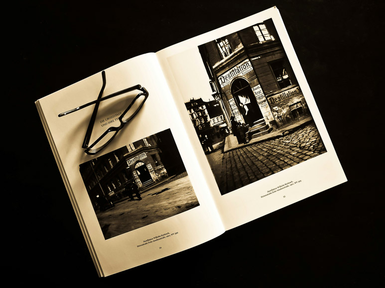 Open book on a table with black and white photographs, accompanied by a pair of eyeglasses placed on top.