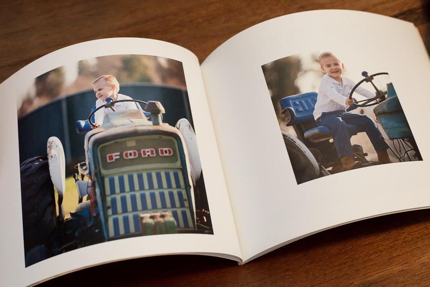 A photo book open to two pages featuring images of a young boy sitting on a vintage tractor outdoors.