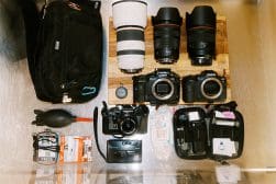 A collection of professional photography equipment laid out on a wooden surface, including cameras, lenses, and accessories.
