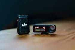 Two compact black DJI audio devices on a wooden surface, one with a screen displaying settings and one with a logo visible.