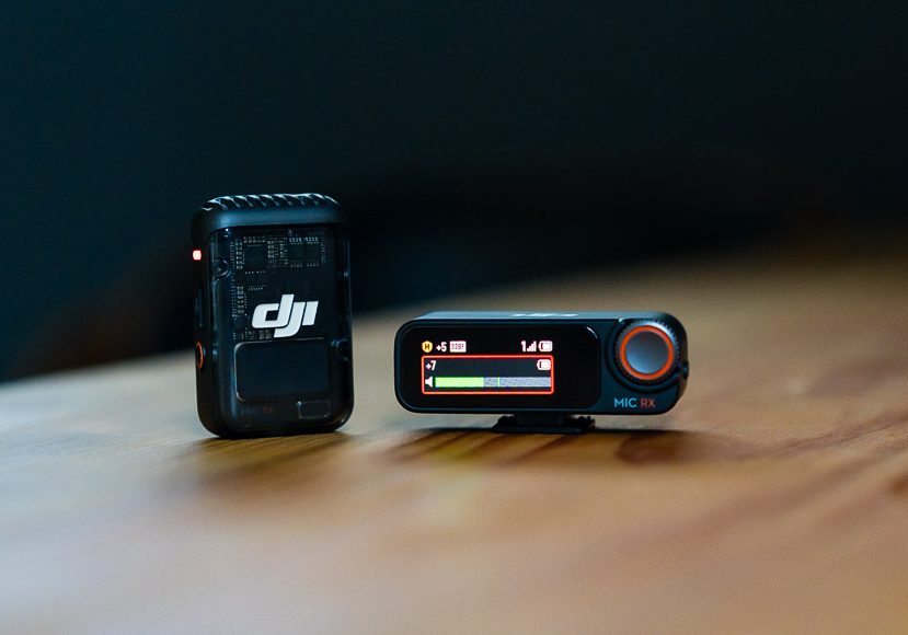 Two compact black DJI audio devices on a wooden surface, one with a screen displaying settings and one with a logo visible. Two compact black DJI audio devices on a wooden surface, one with a screen displaying settings and one with a logo visible.