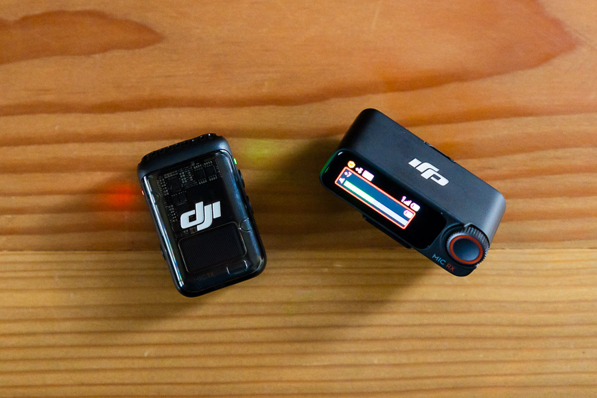 Two compact DJI action cameras are placed on a wooden surface. One camera is upright with its screen on, while the other is lying flat.