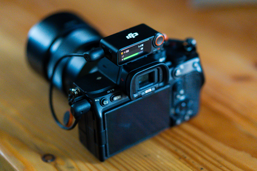 A digital camera with an attached microphone sits on a wooden surface.