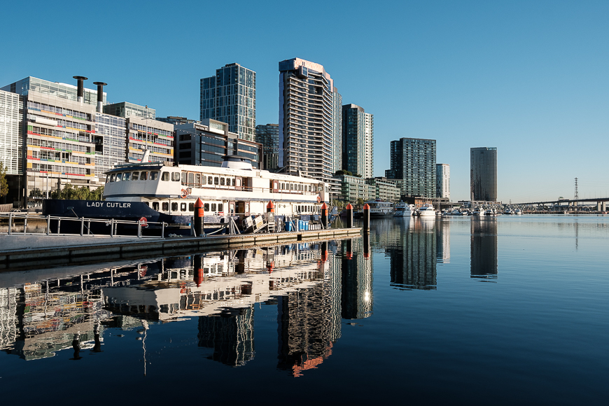 Boat named "lady cutler" docked at a harbor with modern high-rise buildings in the background and clear reflections in the calm water.