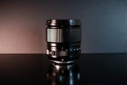 Camera lens placed on a shiny surface against a dark background, with focus markings visible.
