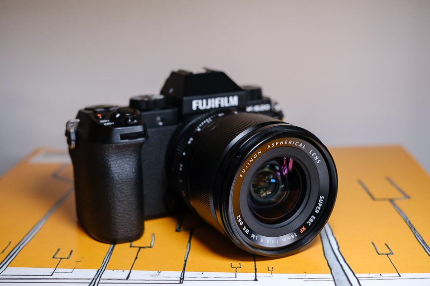 A fujifilm camera with a lens, placed on a yellow surface decorated with geometric lines.