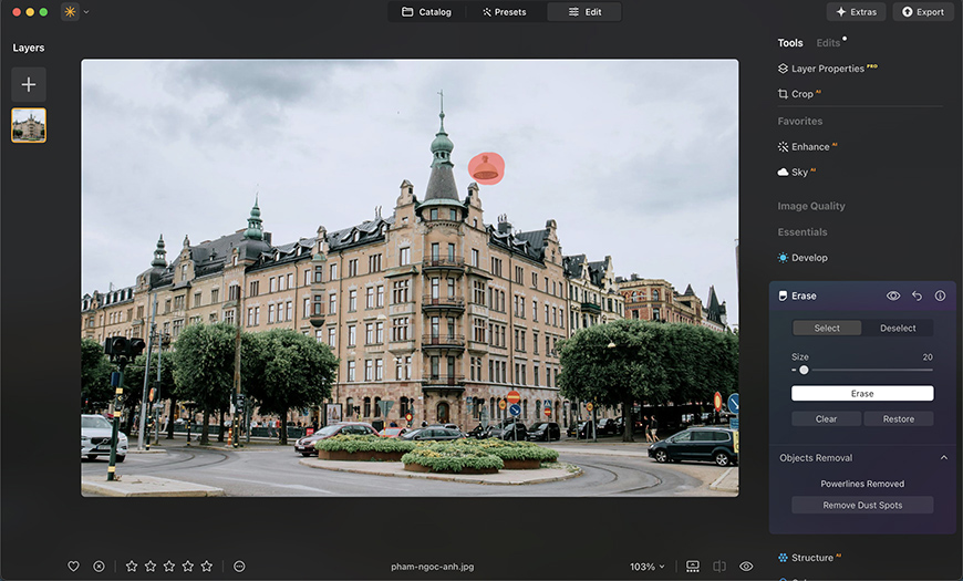 Editing software interface showing a photo of a historic building with a roundabout in front. The eraser tool is selected, highlighting a small area in the sky for editing.