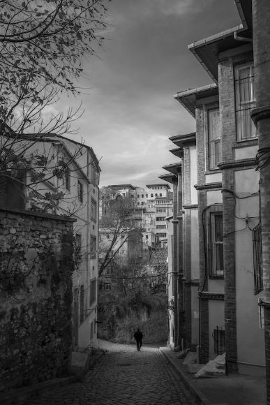 A person walks down a cobblestone street lined with old buildings on a cloudy day.