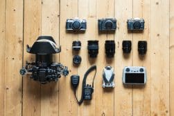 An overhead view of photography equipment arranged on a wooden floor, including cameras, lenses, a drone, a controller, and communication devices.