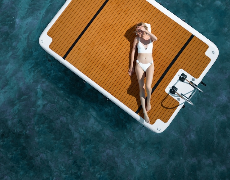 A person in a white swimsuit lounges on a floating platform surrounded by clear turquoise water.