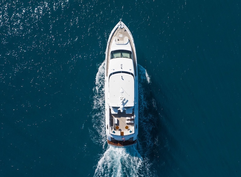 Aerial view of a white yacht cruising through deep blue water, creating waves around its hull.