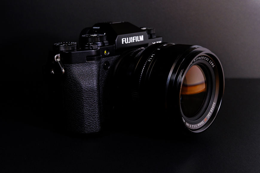 A black fujifilm camera with a fujinon lens, positioned on a dark surface against a black background.