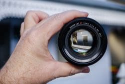 A hand holding a camera lens through which an inverted image of a building is visible.