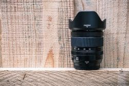 A Fujifilm camera lens with a hood, standing upright on a wooden surface.
