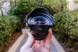 A hand holding a fujifilm camera lens with foliage and a path in the background.