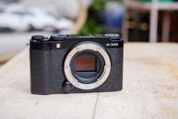 A digital mirrorless camera without a lens is placed on a wooden surface.