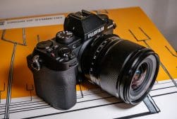 A fujifilm camera with a lens attached, resting on a patterned surface.