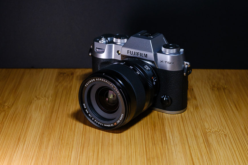 A Fujifilm X-T30 camera with a Fujinon lens is placed on a wooden surface with a dark background.