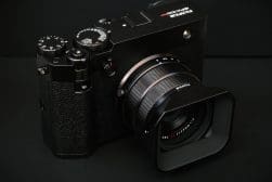 A black Fujifilm digital camera with a large lens and various controls rests on a black surface.