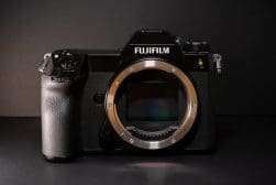 A Fujifilm mirrorless digital camera without a lens attached, showing the sensor, on a black background.