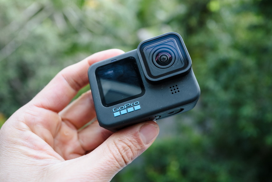 A hand holding a GoPro action camera against a blurred green background.
