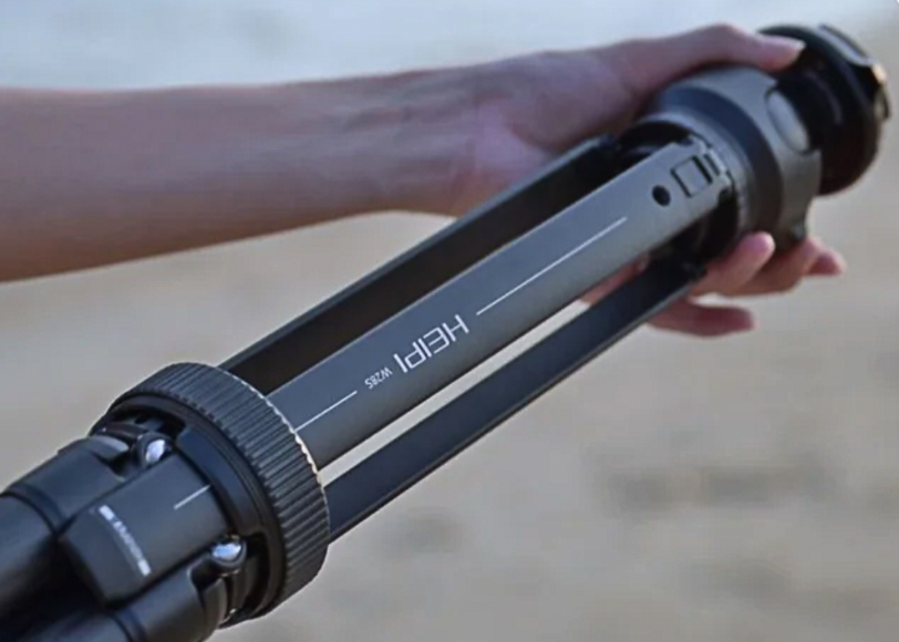 A person holding a black tripod with "HERI" printed on it.