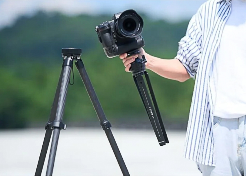 Person adjusting a camera on a tripod with an outdoor background.