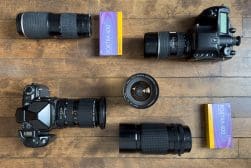 Cameras and lenses arranged on a wooden surface, accompanied by two Kodak Portra 400 film boxes.