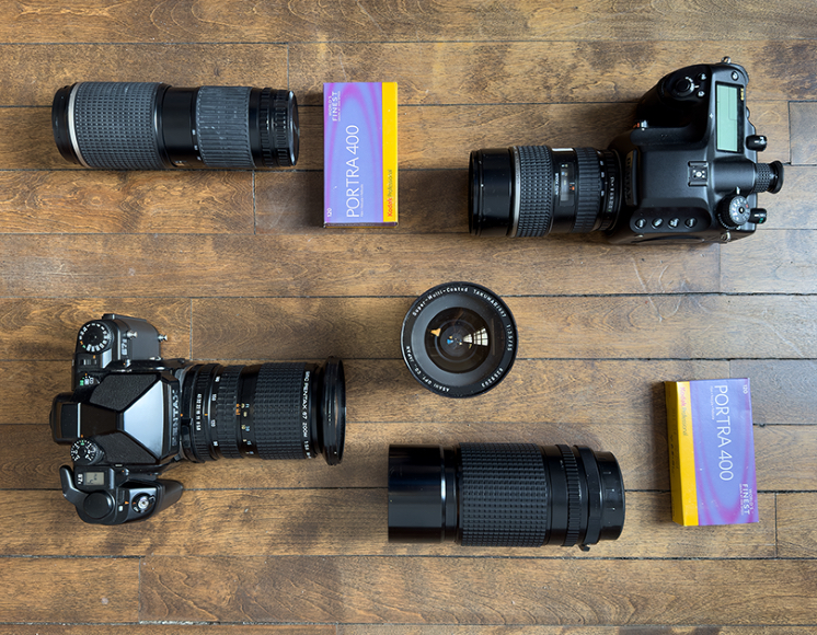 Cameras and lenses arranged on a wooden surface, accompanied by two Kodak Portra 400 film boxes.