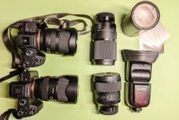 Two Sony cameras with various lenses and a Godox flash are laid out on a light green surface.