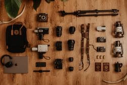 A laptop, camera, and other items are laid out on a wooden floor.