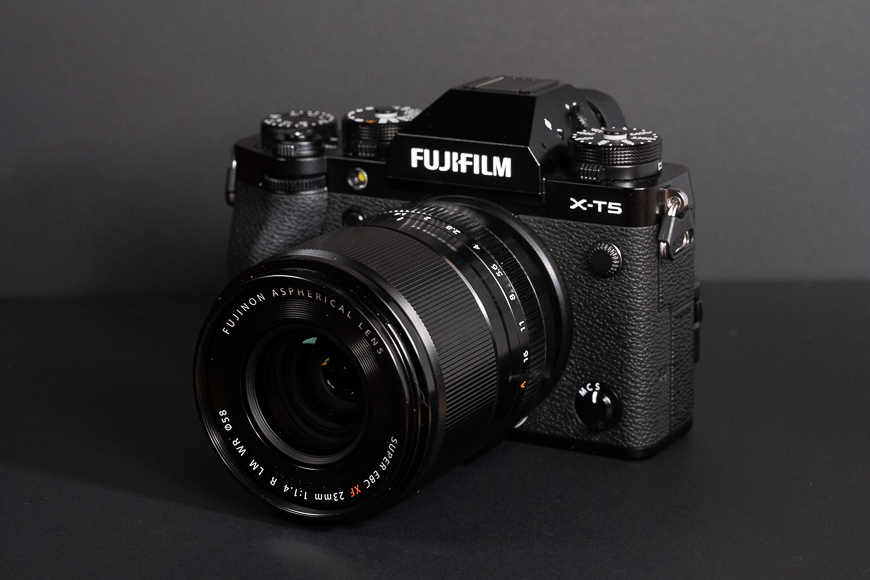 A black Fujifilm X-T5 mirrorless camera with a mounted lens is placed against a dark background.