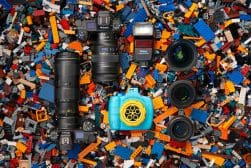 A collection of photography equipment, including cameras, lenses, and a flash, laid out on a colorful background of assorted lego bricks.