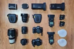 A variety of camera equipment, including lenses, two cameras, flash units, and accessories, arranged neatly on a wooden floor.