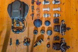 Aerial view of assorted photography equipment arrayed on a wooden floor, including cameras, lenses, and accessories.